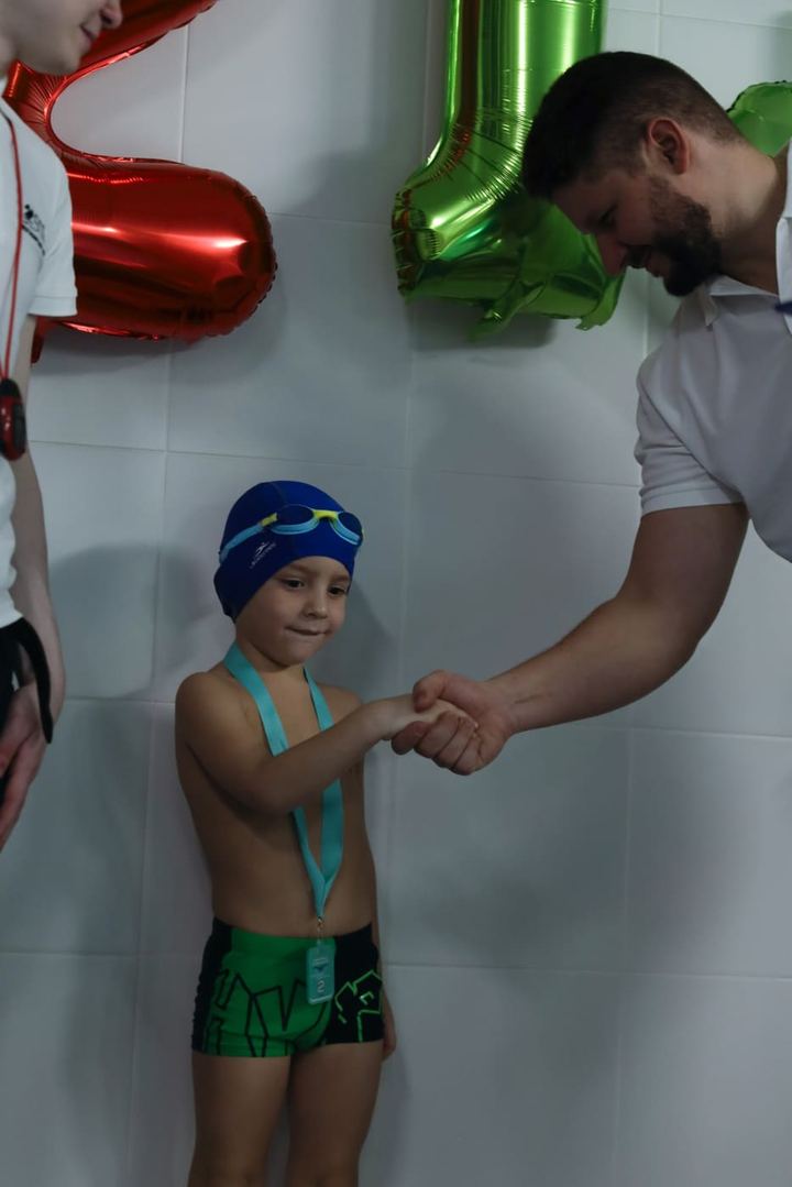 Тренер пожимает руку юному пловцу с медалью после соревнований
