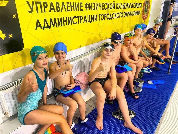 Группа юных пловцов с ластами показывает большой палец у бортика бассейна